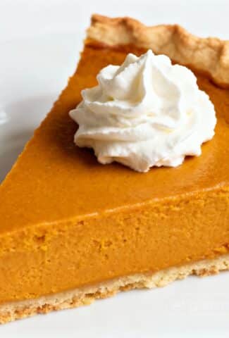 Slice of pumpkin pie with whipped cream on white plate.